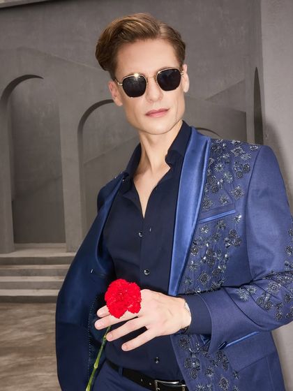 The embroidered navy tuxedo seen from another angle, showcasing its modern silhouette and confident style. The open jacket reveals the quality of the inner lining and the overall relaxed fit.