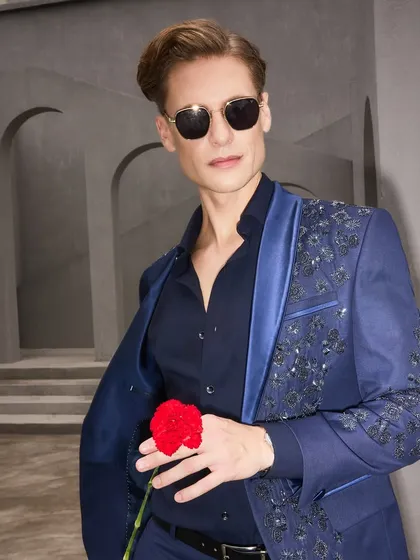 The embroidered navy tuxedo seen from another angle, showcasing its modern silhouette and confident style. The open jacket reveals the quality of the inner lining and the overall relaxed fit.