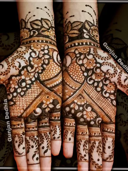 A full-coverage Indian mehendi design. The pattern combines floral elements, peacock motifs, and leafy vines on the fingers for a dense and beautiful look.