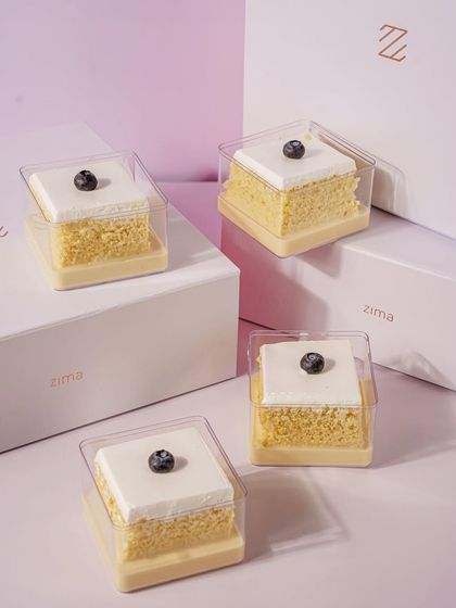 Simple, elegant, and clean. This shot of mini tres leches cakes in their individual packaging highlights the product's quality and sophisticated branding. The composition is balanced and pleasing to the eye, perfect for a premium bakery.