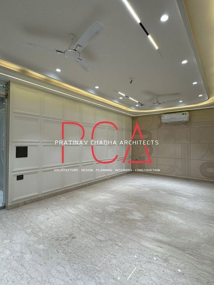 A spacious living area in Vasant Kunj defined by its clean lines and elegant wall treatments. One wall features classic white moulding, while the other has a custom CNC-carved panel, showcasing a blend of different styles.