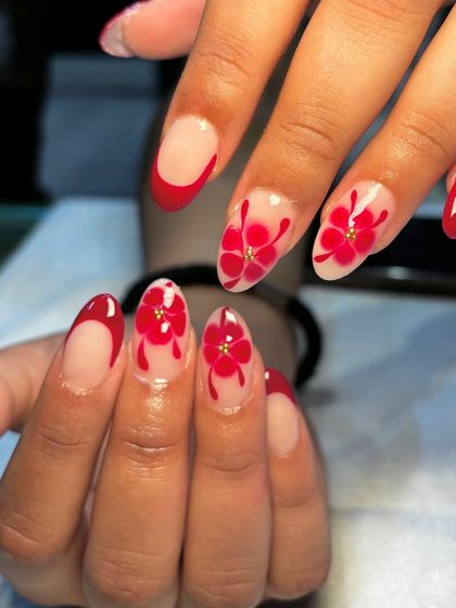 Let your nails do the blooming with this vibrant red floral design. This look combines a reverse French tip with beautiful, hand-painted red flowers for a bold and feminine statement.