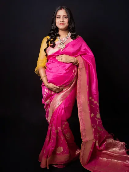 A simple, elegant portrait of a mother-to-be cradling her bump in a beautiful pink saree. Her serene expression captures the quiet joy of pregnancy.