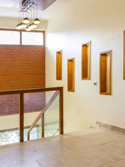 An exposed brick wall serves as a textured backdrop for the upper floor landing. The wooden niches are designed for displaying art, adding a personal touch to the space.