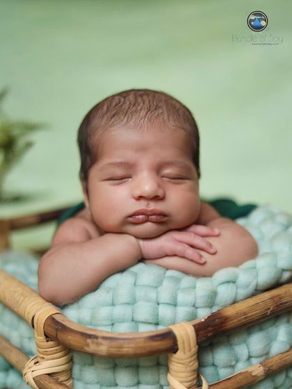 A "tummy time" pose showing a newborn resting his chin on his hands at the edge of a basket, a perfect way to capture their chubby cheeks and pouty lips.