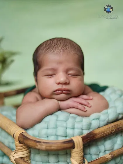 A "tummy time" pose showing a newborn resting his chin on his hands at the edge of a basket, a perfect way to capture their chubby cheeks and pouty lips.