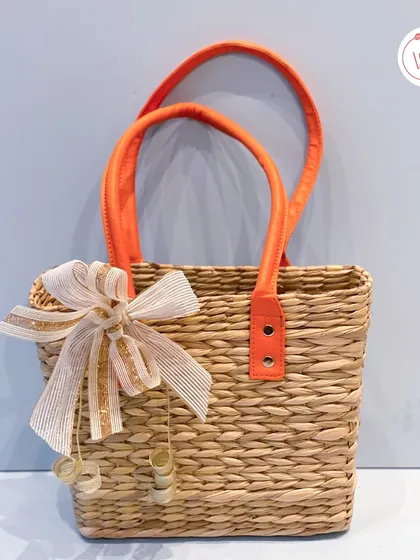 A chic and eco-friendly jute bag with bright orange handles, perfect for a mehendi or haldi favor bag.