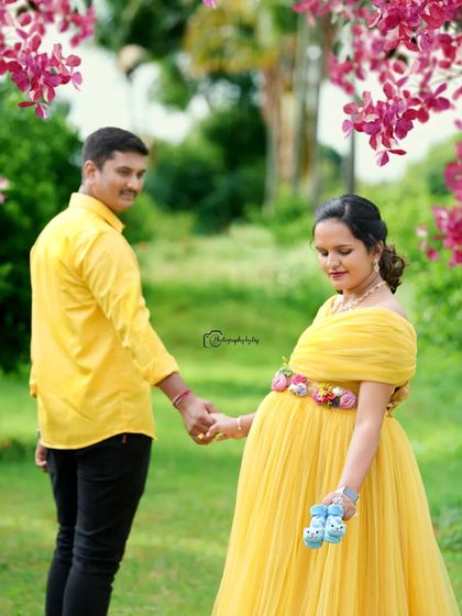 A sweet couple's portrait in a garden, holding tiny baby shoes. The mother-to-be is wearing a yellow gown.