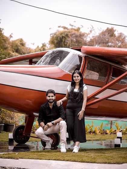 A stylish couple poses by the red airplane, a unique and impressive backdrop for any photoshoot.