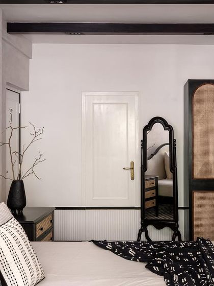 This bedroom in the "Getaway to Galle" home features a black-framed bed and a stunning black wardrobe with arched cane panels, creating a bold yet tropical feel.