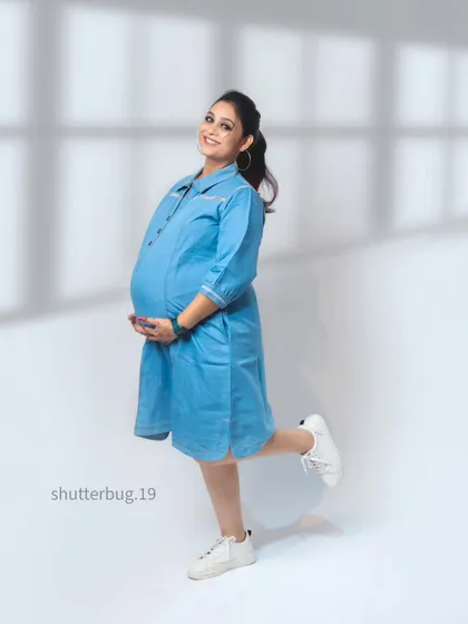 A cheerful and casual solo portrait of the mom-to-be in a cute denim dress. This shot complements the "Vogue cover" concept, showing a more relaxed but equally stylish side.