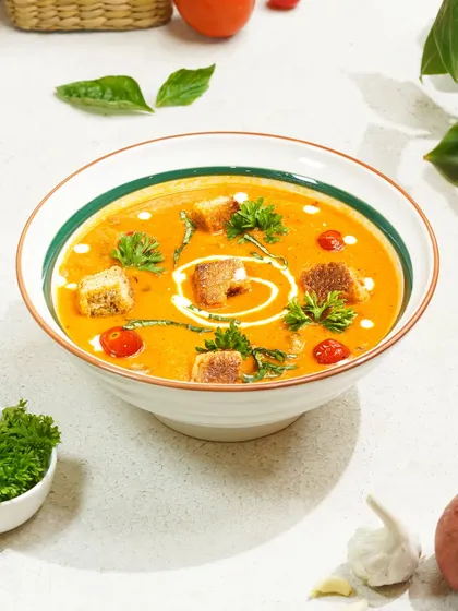 A classic, comforting bowl of tomato soup with croutons, styled with fresh herbs to look both simple and elegant.