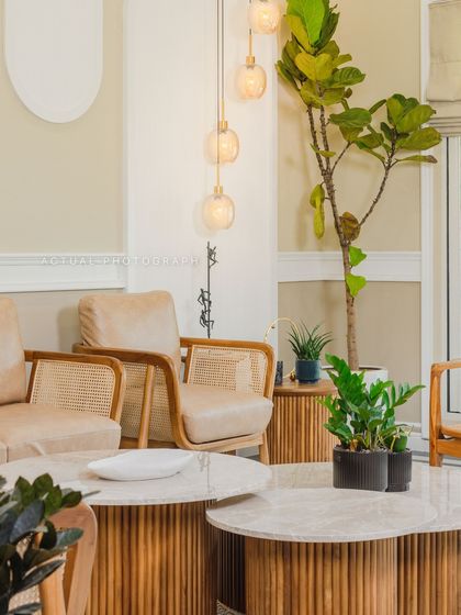 This living area detail shows the interplay of textures, from the fluted wood coffee tables to the cane-back armchairs and lush indoor plants, creating a warm and organic modern space.