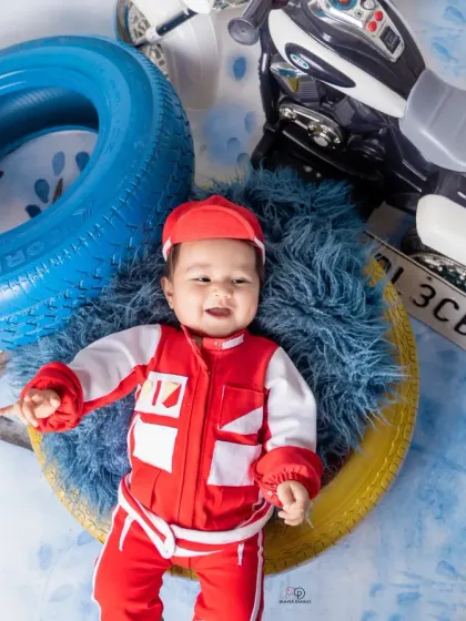 A few action shots from an F1 and racing-inspired photoshoot. The baby is styled in a red racing uniform, captured with fun expressions among tires and toy vehicles.