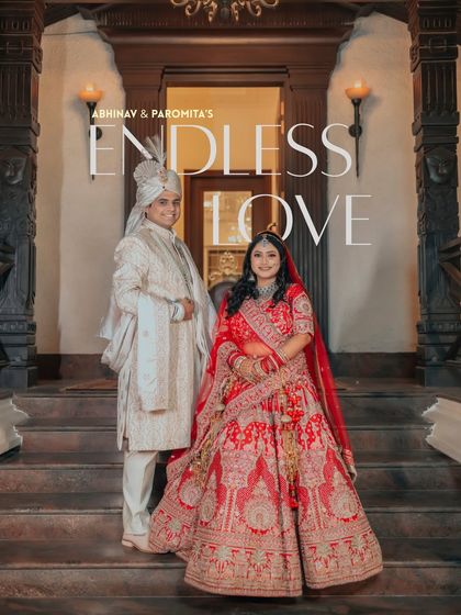 A regal portrait of Abhinav and Paromita, titled 'Endless Love.' Their traditional red and white outfits stand out against the classic architectural backdrop.