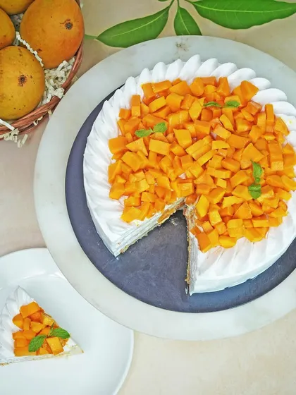 An overhead view of a whole mango cake with a slice taken out, showcasing the generous fruit topping. This composition is great for websites and banners, giving a complete view of the product.