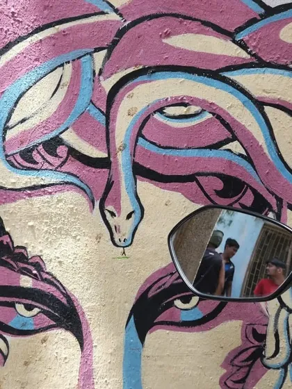 A creative photograph of the Medusa mural, using a scooter's rearview mirror to capture the reflection of passersby. The shot cleverly frames life within the art.
