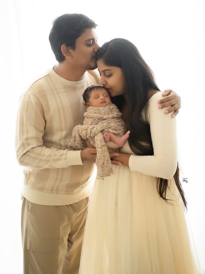 A portrait of pure love, with both parents kissing their sleeping baby. The soft, high-key lighting and neutral tones give this image a dreamy, ethereal quality.
