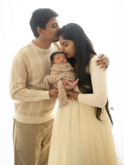 A portrait of pure love, with both parents kissing their sleeping baby. The soft, high-key lighting and neutral tones give this image a dreamy, ethereal quality.