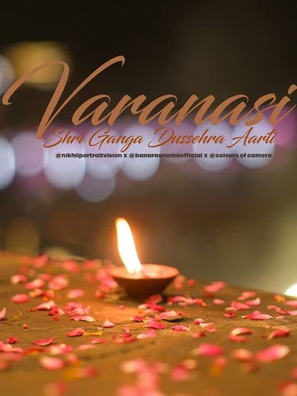 A single diya rests on a bed of flower petals, with the blurred lights of Varanasi in the background. This artistic shot captures the quiet, personal moments of devotion.