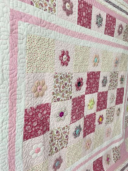 An angled view of the pink hexagon quilt, showing the texture of the quilting and the appliquéd flowers.