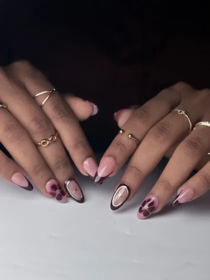 A sophisticated set featuring a deep wine-colored French tip, a hand-painted abstract floral, and a gold-rimmed negative space nail.