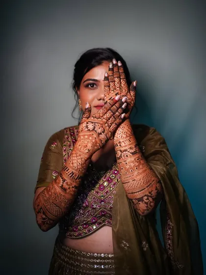 A playful portrait of the bride peeking through her henna-covered hands. This shot is both creative and a great way to showcase the detailed mehndi art.