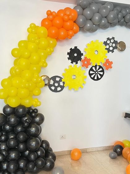 A creative construction-themed balloon arch using black, yellow, and orange balloons to simulate smoke, with gear cutouts on the wall.