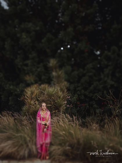 A bride stands amidst tall grasses, creating a portrait that feels both grand and connected to nature. The soft focus adds a touch of mystery and elegance.