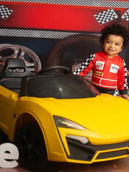 A proud one year old standing by his cool yellow car. The racing flags and balloons complete this fun and dynamic setup.