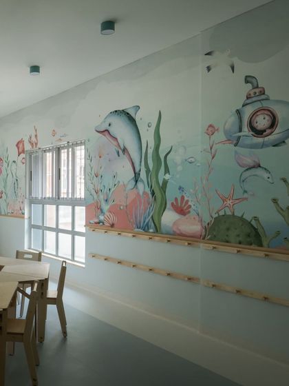 A submarine and a smiling dolphin are part of the custom wallpaper in the aqua classroom. The long wooden peg rail provides ample storage for the children's belongings, keeping the space tidy.