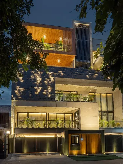 This residential facade embodies a contemporary aesthetic with its clean lines and distinct volumes. The interplay of 3D geometric patterns on stone cladding and warm wooden panels creates a striking modern look, enhanced by strategic lighting and integrated planters.