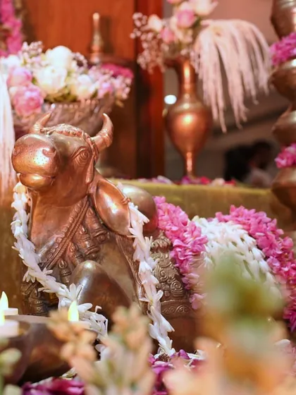 A close up of a brass Nandi statue, adorned with a garland of fresh flowers. This traditional element adds a sense of sanctity and completeness to the Hindu puja decoration.