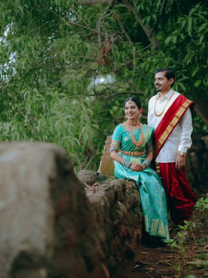 A beautifully composed portrait of the couple in a natural setting. The bride is seated while the groom stands, creating a classic and elegant pose.