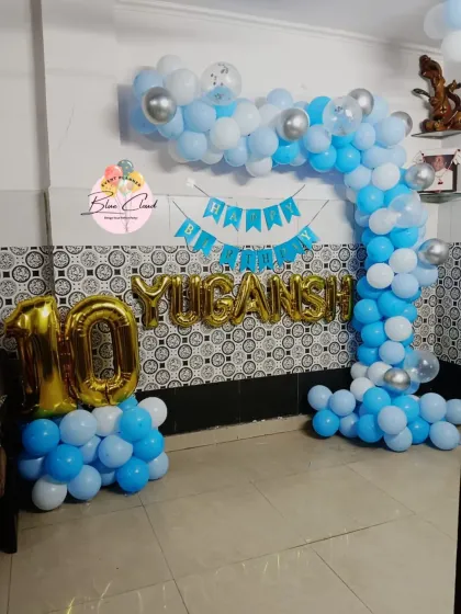 A blue and white balloon arch with the name 'YUGANSH' in foil letters for a 10th birthday.