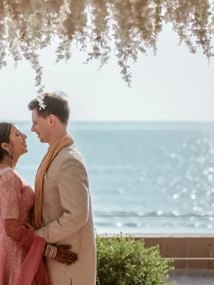 A beautiful portrait of a couple by the sea, framed by hanging floral decorations. This image perfectly combines the romance of the couple with the beauty of a beachside wedding setup.