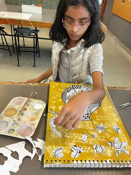 This student is arranging her black and white cut-outs onto a painted yellow background, creating a dynamic still life collage.