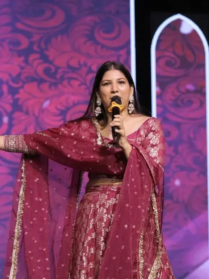 A wide shot of me hosting on stage, with a vibrant floral background on the LED screen. The visual production of a Sangeet is key to its success.