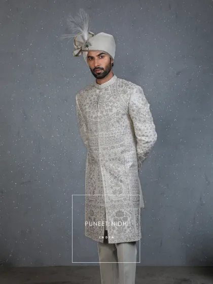 An ivory-toned silk sherwani adorned with Resham embroidery, where a floral and vine jaal meets geometric lattice patterns. This is a regal harmony of tradition and modern elegance, crafted for the big day.