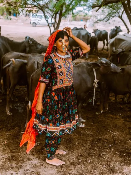 A Dhaneta Jat woman stands with her herd of buffaloes. This image shows her in her daily environment, connecting her traditional attire with her pastoral way of life.