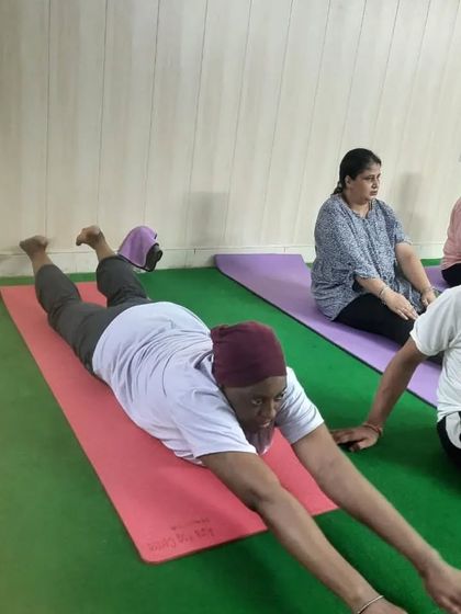 A student practices a variation of Salabhasana (Locust Pose), a great asana for strengthening the back and improving posture, with an instructor nearby.