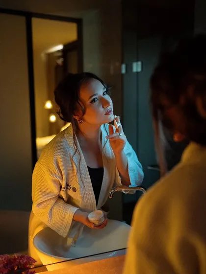 A portrait captured through a mirror reflection. The warm, soft lighting and the model's gentle expression create a quiet, intimate scene of self-care.