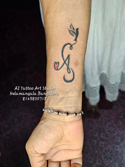 An initial 'A' tattoo with a heart and a bird taking flight, a very creative and personal design.
