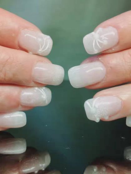 A delicate and sheer white manicure with subtle 3D sculpted bow details on the accent nails.