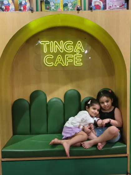 Two sisters cuddle up in the green booth at Tinga Cafe after a day of play.