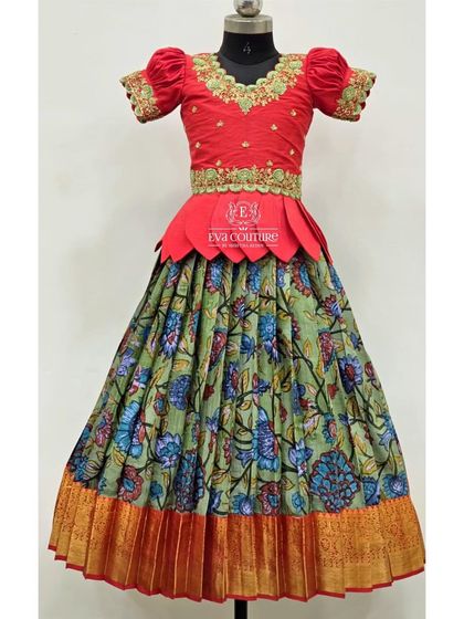 A Kalamkari print lehenga in green and blue, paired with a bright red blouse. The blouse has a petal-style peplum and intricate embroidery.