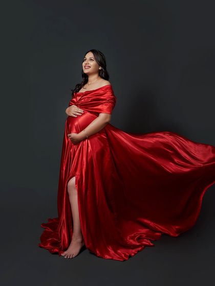 A stunning studio maternity portrait. The 'Scarlet' gown in vibrant red satin is styled for maximum drama, with the fabric flowing beautifully for a powerful, artistic shot.
