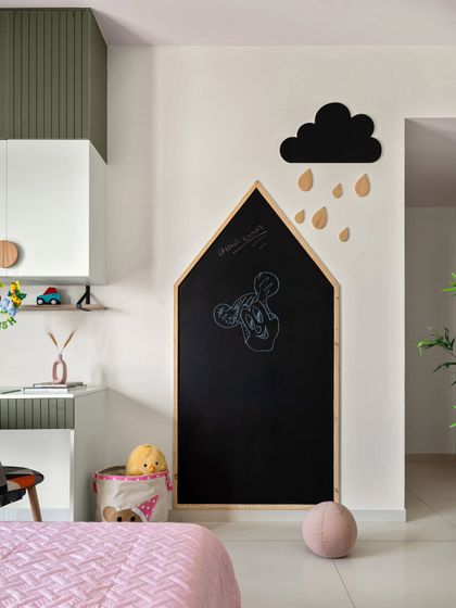 This kids' room features a whimsical house-shaped chalkboard, perfect for unleashing creativity. The study area combines olive green and white cabinets with circular wooden knobs for a playful yet stylish look.
