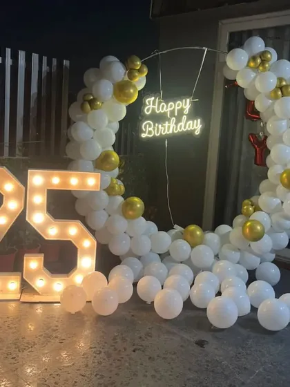 A clean and elegant 25th birthday setup. The white and gold balloon ring, neon sign, and light-up numbers are perfect for a sophisticated party on a terrace.