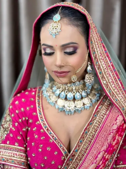 A vibrant and modern bridal look featuring a hot pink lehenga and contrasting light blue jewelry. The eye makeup has hints of purple and silver for a dramatic effect.